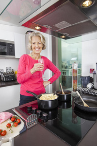 快乐老太太在厨房里用香槟杯烹调食物的画像