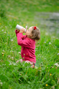 那个女孩从热水瓶喝水。杯子热水瓶 春草 卷曲的头发 户外娱乐 健康的生活方式 环境保护 保护自然，有意识的消费