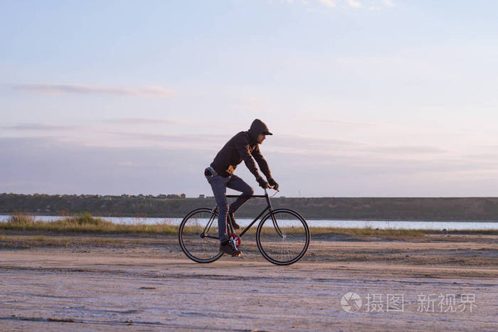 独自骑固定齿轮公路自行车骑河,时髦旅游自行车骑手图片附近的沙漠