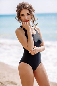 高级时装 look.glamor 美丽时尚黑发年轻女模特与明亮的化妆，用完美的日光浴皮肤干净的黑色泳装时尚风格在海滩上