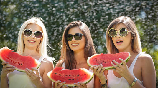 带着太阳眼镜吃新鲜西瓜和微笑的美丽女孩。幸福的年轻女人，在公园里吃西瓜。青年人的生活方式。幸福 喜悦 夏天的概念