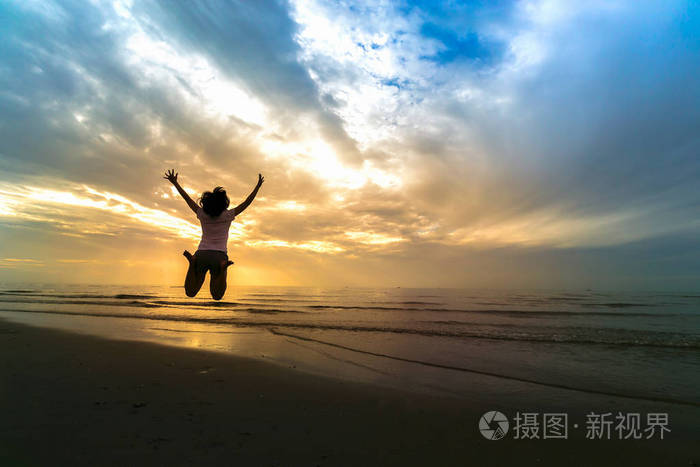女人在日落在海边的沙滩上跳跃自由生活的概念