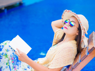 夏天的帽子，躺在躺椅上，读一本书，在游泳池畔的女人。假期和松弛，夏天旅游概念