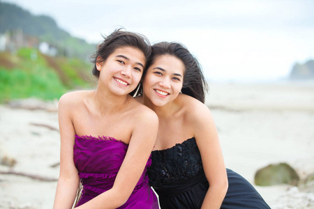 两个十几岁的女孩，在优雅的礼服在海滩上一起微笑