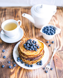 煎饼与蓝莓 沼泽 whortleberry 杯绿茶 蓝莓和棕色木制背景上的茶壶杯健康早餐