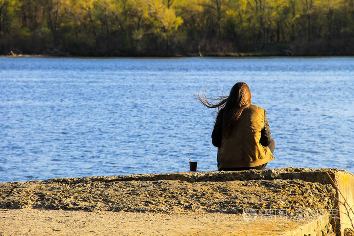 年轻女子独自一人坐在码头上杯咖啡