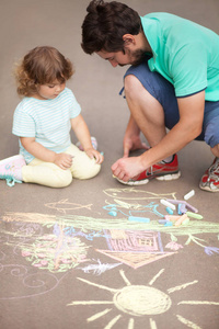 可爱的蹒跚学步的女孩和她的父亲用彩色粉笔绘制