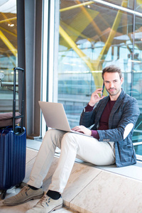 男子坐在机场使用笔记本电脑和手机旁边