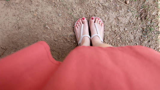 在土壤背景下, 亲密的女孩脚上穿着凉鞋和红指甲