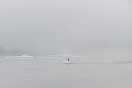潜水服坐在雾期待着海洋的海滩上的冲浪者