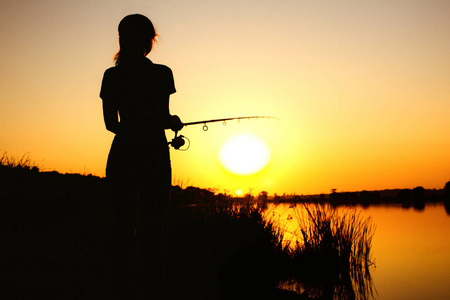 一个钓鱼妇女的剪影在河岸在自然在黎明
