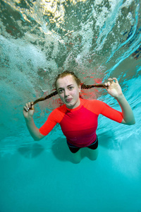 年轻的运动型女孩是在蓝色背景的红色泳衣水下游泳，看着我，微笑着