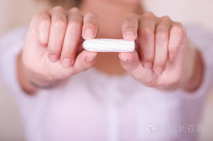 一个年轻的女人在她面前指月经棉卫生棉条模糊的背景中的特写