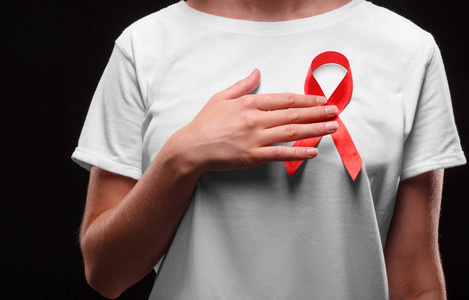 一位女性在黑色背景上的白色 t 恤上的红丝带。现代治疗和保健。艾滋病意识概念