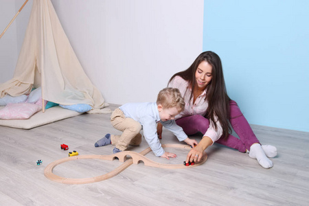年轻快乐的妈妈，小儿子玩木铁路在地板上
