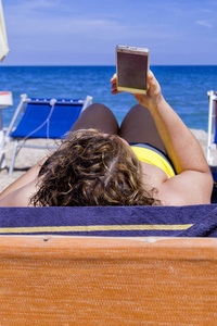 女孩看着智能手机在海滩上与大海为背景。弛豫和通信的概念