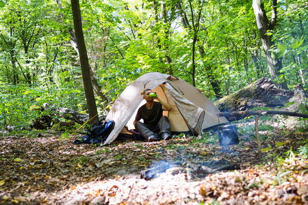 在森林里的篝火和一个旅游帐篷, 游客在帐篷附近休息