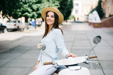 年轻的女人坐在摩托车踏板车在老城狭窄的街道上