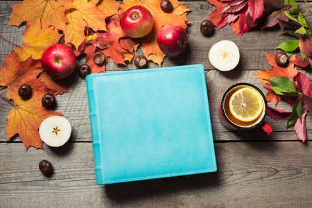 秋天的概念。蓝色册页以文本和杯茶空间，装饰秋天的叶子，木板上的苹果