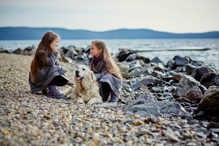 两个小的孪生姐妹散步和在海滩上的狗
