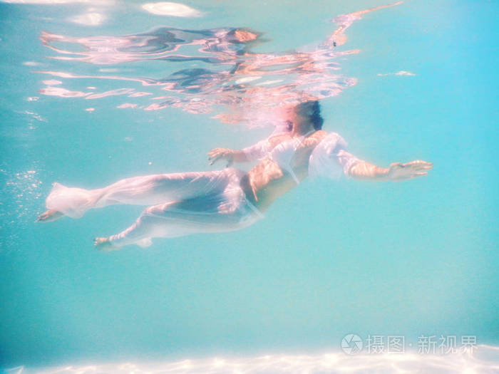 女人美丽的身体在水下游泳时穿白色礼服