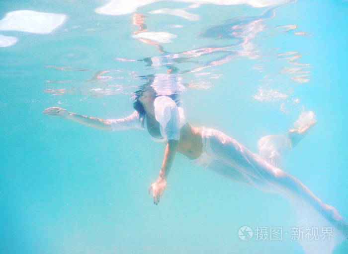 女人美丽的身体在水下游泳时穿白色礼服
