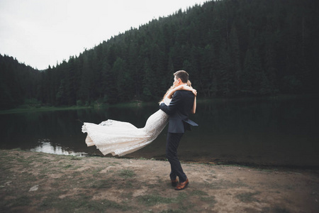 年轻新婚夫妻，新娘和新郎接吻 拥抱完美观的山，蓝色的天空
