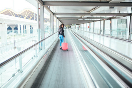 在机场的一个粉红色的手提箱的移动人行道的黑女人