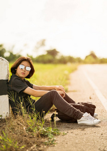 女人坐在乡村路上搭便车，背包里