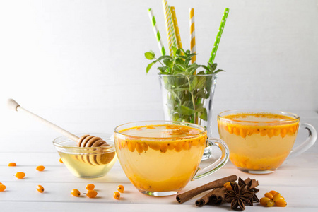 维生素健康沙棘茶在玻璃杯与新鲜的原始沙棘浆果和肉桂棒, 八角, 薄荷和蜂蜜