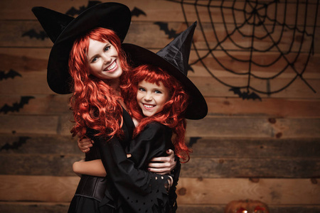 万圣节的概念   美丽的白人母亲和她的女儿长长的红头发在女巫服饰快乐微笑和拥抱彼此