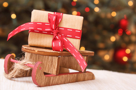 用木制雪橇和背景灯的圣诞树上的丝带包装的礼品