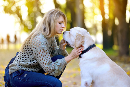 金发女郎玩她的拉布拉多猎狗在秋天的公园