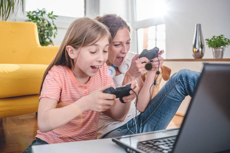母亲和女儿在家里用笔记本电脑玩电子游戏