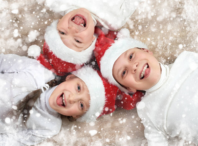 快乐的孩子在一起躺在木制的背景下，身着圣诞圣诞老人的帽子和乐趣，冬天假日概念，雪装饰
