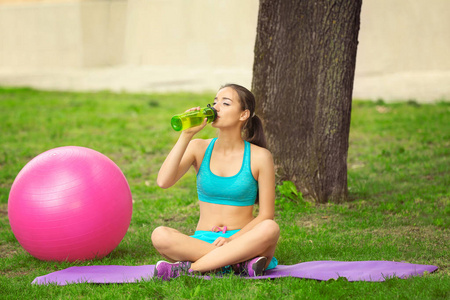 年轻运动的妇女喝凉水坐在草地上的绿色公园