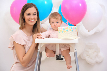 母亲靠近可爱的小女孩，带着美味的蛋糕和装饰，背景是生日聚会