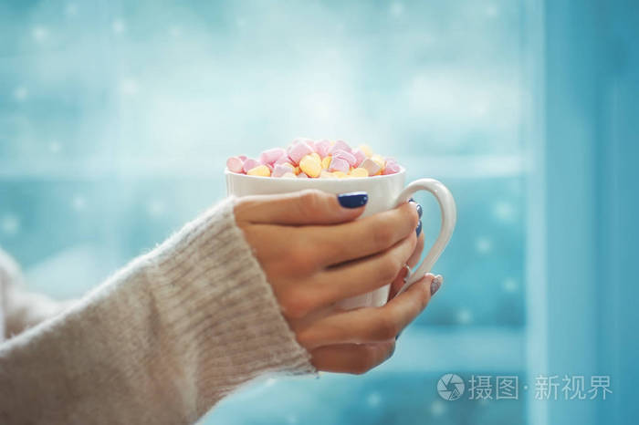 关在年轻女人女手以修指甲捧着一杯热可可, 棉花糖或咖啡室内雪蓝色