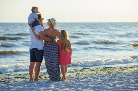 父亲母亲和两个女儿站在沙滩上欣赏大海