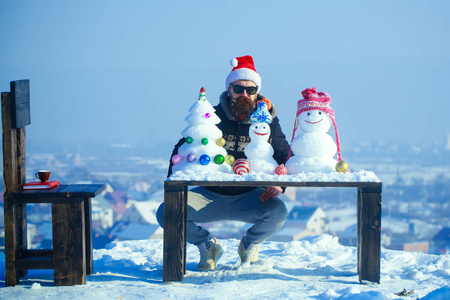 赶时髦的人坐在一起堆雪人和雪圣诞树上表