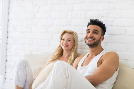 年轻夫妇坐在枕头地板上, 快乐的微笑拉美裔男子和妇女恋人在卧室
