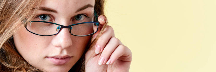 漂亮的红发女郎十几岁的女孩有雀斑戴上阅读眼镜，微笑在黄色背景上的少女肖像