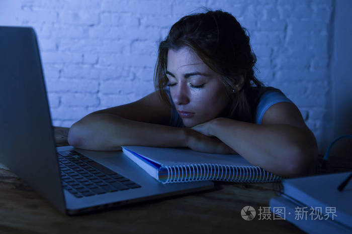年轻美丽和疲倦的学生女孩睡觉小睡躺在家里笔记本电脑办公桌疲惫和