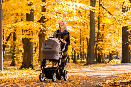 一个年轻母亲与婴儿小推车走过秋天的公园