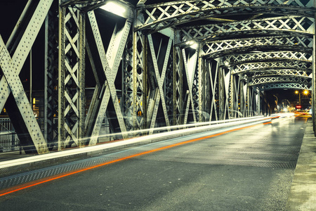 在城市的一座桥梁的钢建筑下的沥青路。夜晚的城市景象, 在隧道中有汽车灯的踪迹。调子