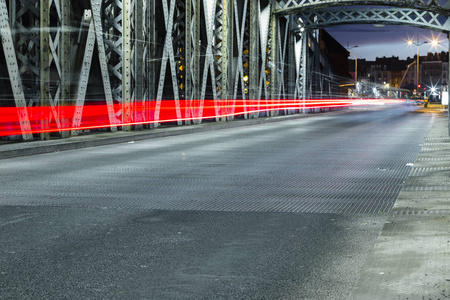 在城市的一座桥梁的钢建筑下的沥青路。夜晚的城市景象, 在隧道中有汽车灯的踪迹。调子