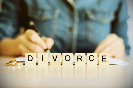 字离婚由桌子上的木制字母和结婚戒指组成。 在一位年轻白人妇女的背景下签署离婚协议