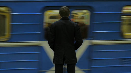 在地铁站后面拍摄的孤独青年男子的后视图添加看手表等待火车。商人在驻地