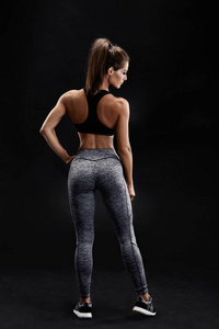 一个坚强的女人，与肌肉腹部在运动服的镜头。黑色背景下的健身女模特