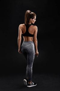 一个坚强的女人，与肌肉腹部在运动服的镜头。黑色背景下的健身女模特